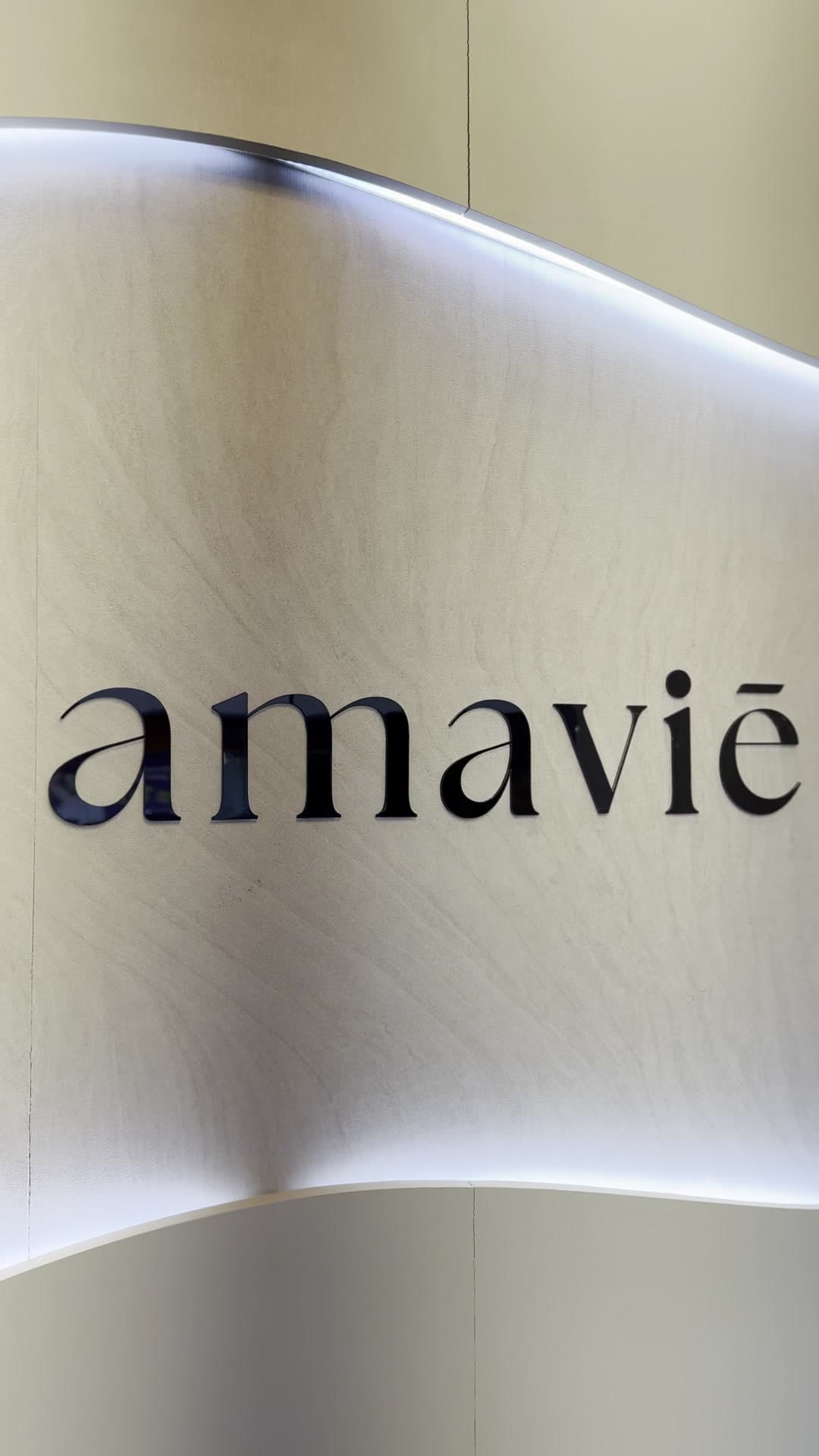 Parede curva retroiluminada com o logotipo amaviē na recepção da clínica Amaviē Estética Inteligente, Kobrasol, São José/SC